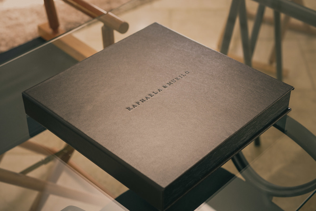 O álbum de casamento da Raphaela e do Murilo, teve uma caixa em couro legítimo, com os nomes gravados em baixo relevo. Na parte interna, uma bolsa em revestimento soft-touch, capa e contra-capa em papel fotográfico canvas e interior em papel seda. 