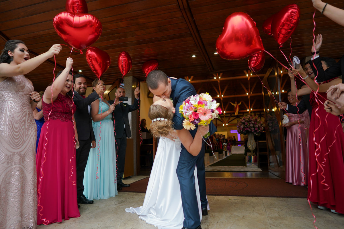Casamento dos noivos Francine e Rodrigo realizado em Curitiba, com festa no restaurante Madalosso, fotografado pelo melhor fotógrafo de casamentos de Campo Largo e Curitiba, Michel Druziki. Noivos se beijando na saída da igreja com balões de coração