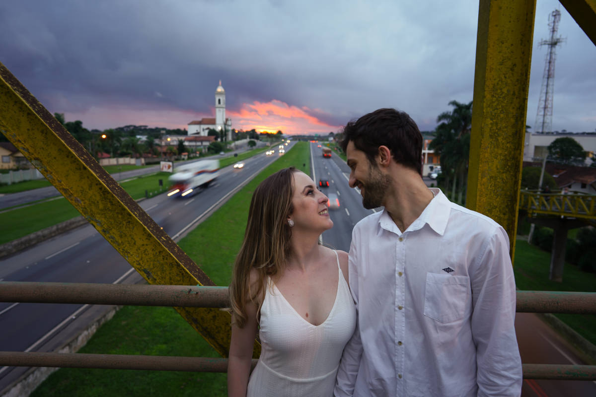 Ensaio de casamento do casal Camila e Guto fotografado pelo fotógrafo Michel Druziki em Campo Largo. Casal de mãos dadas sorrindo e se olhando em cima da passarela