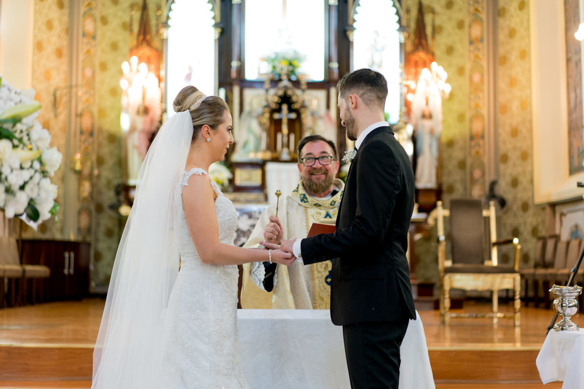 Casamento da Camila e Guto na igreja Matriz de Campo Largo, fotografado pelo melhor fotógrafo de casamentos em Campo Largo e Curitiba, Michel Druziki. Noivos sorrindo no momento da benção do padre