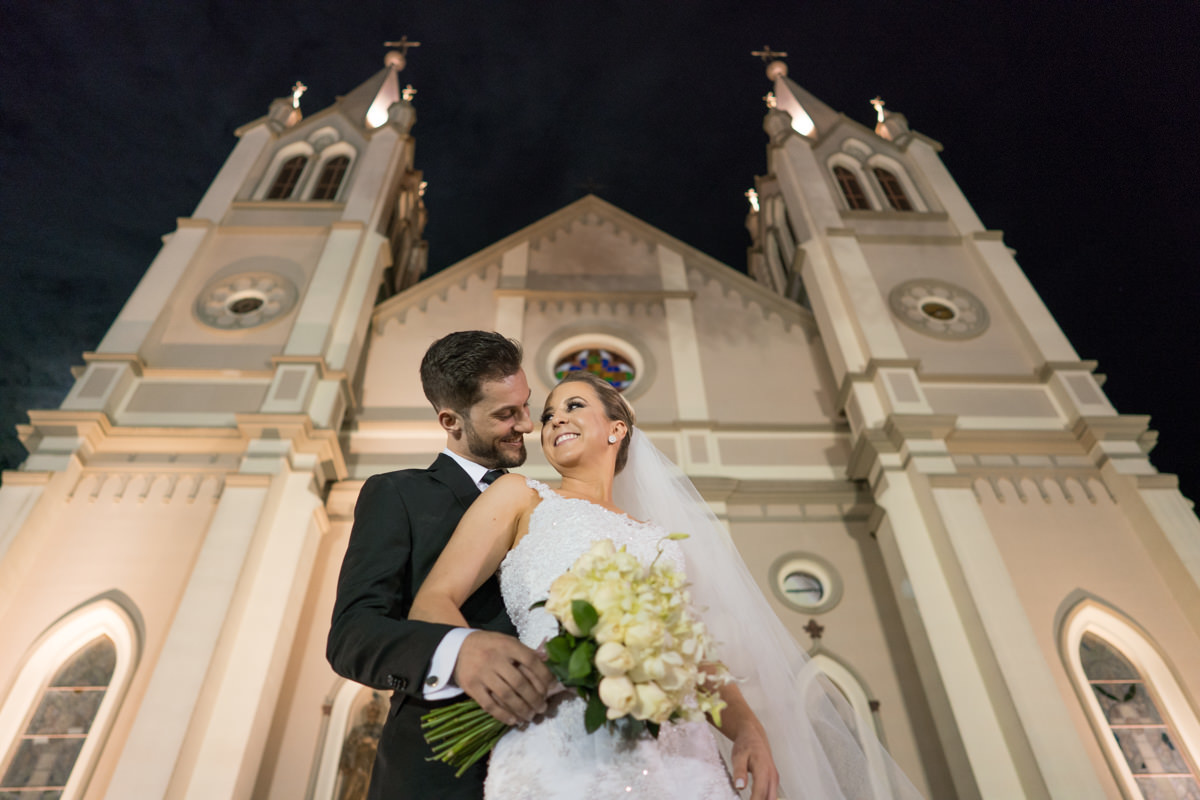 Casamento da Camila e Guto na igreja Matriz de Campo Largo, fotografado pelo melhor fotógrafo de casamentos em Campo Largo e Curitiba, Michel Druziki. Noivos abraçados e sorrindo em frente à igreja