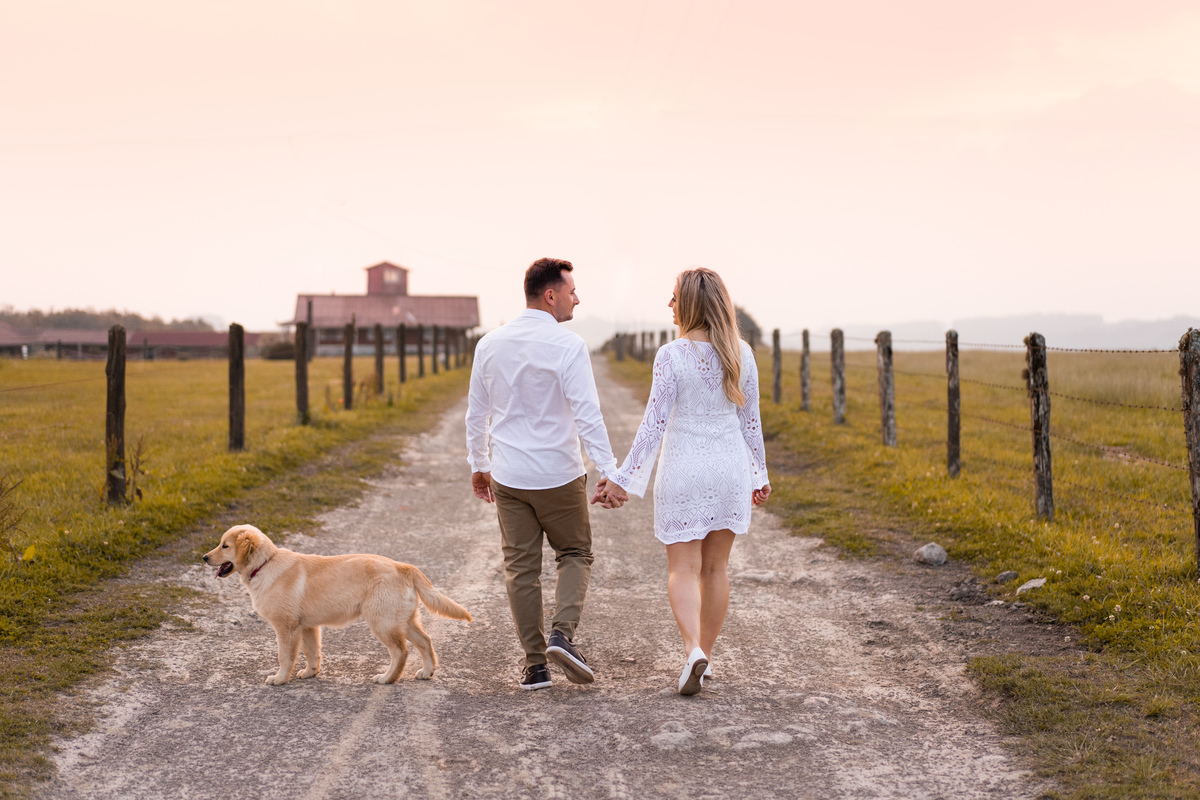 O fotógrafo de casamentos em Campo Largo e Curitiba, Michel Druziki fotografou o casal Ana Maria e Ricardo no Rancho P&R Luxo do Campo em São Luiz do Purunã. Casal de costas  caminhando de mãos dadas no campo com cachorrinho fofo.