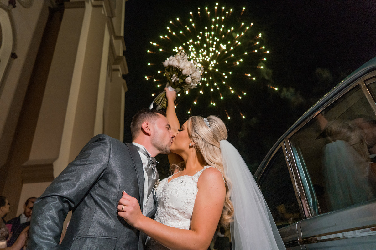 Casamento lindo da Ana Maria e Ricardo, na igreja Matriz, fotografado pelo fotógrafo de casamentos em Campo Largo e Curitiba, Michel Druziki. Noivos se beijando com fogos de artifício ao fundo