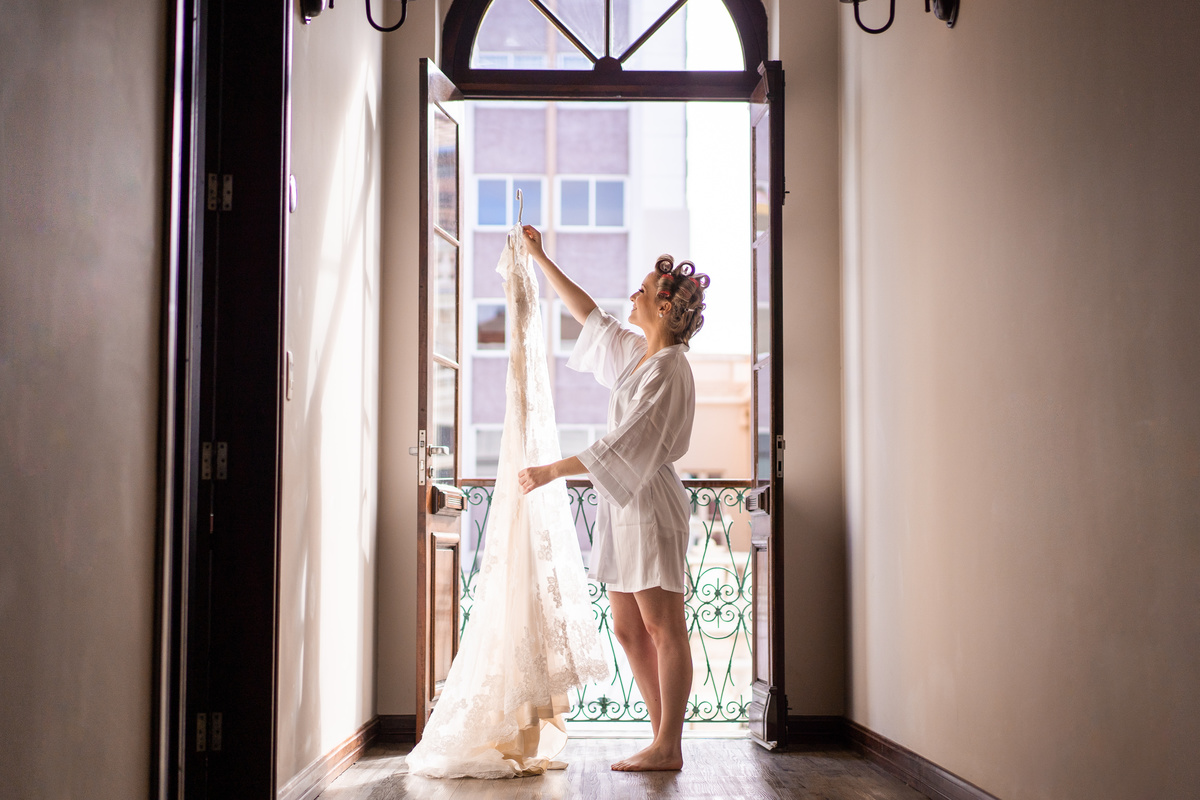 Making of no hotel, feito pelo fotógrafo de casamentos em Campo Largo e Curitiba, Michel Druziki. Casamento Daniela e Paulo, em Curitiba. Noiva olhando para o vestido na varanda. 