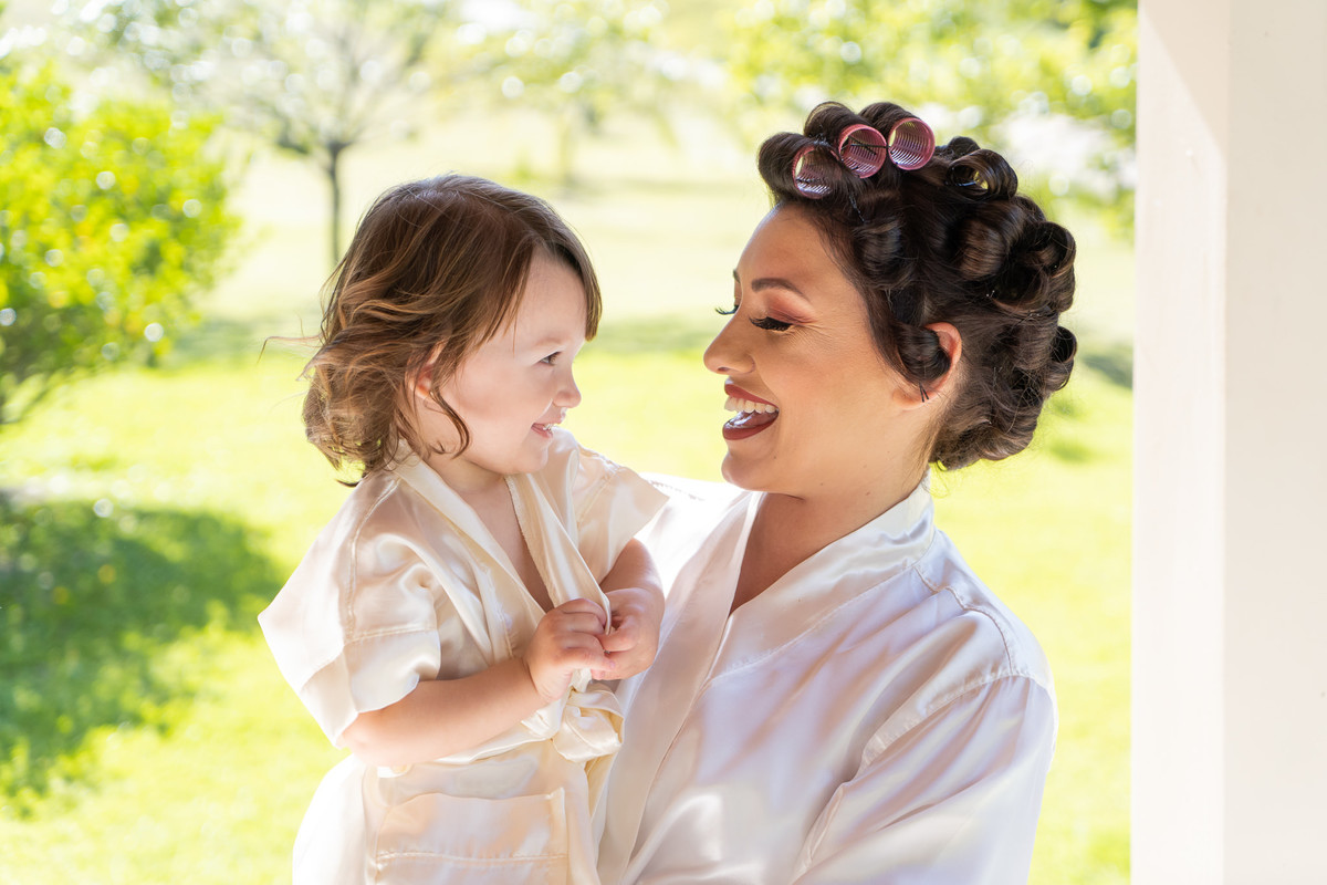 O fotógrafo de casamentos em Campo Largo e Curitiba, Michel Druziki fotografou o casamento de Kaline e Paulo no Espaço Eccos em uma manhã de sábado ensolarada, em Campo Largo. Noiva sorrindo com a filha no colo.