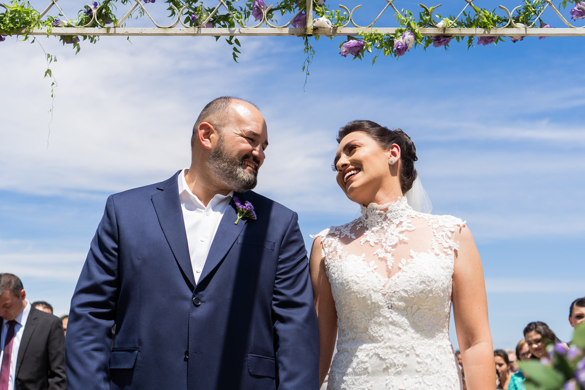 O fotógrafo de casamentos em Campo Largo e Curitiba, Michel Druziki fotografou o casamento de Kaline e Paulo no Espaço Eccos em uma manhã de sábado ensolarada, em Campo Largo. Noivos sorrindo e se olhando durante o casamento de dia, céu azul.
