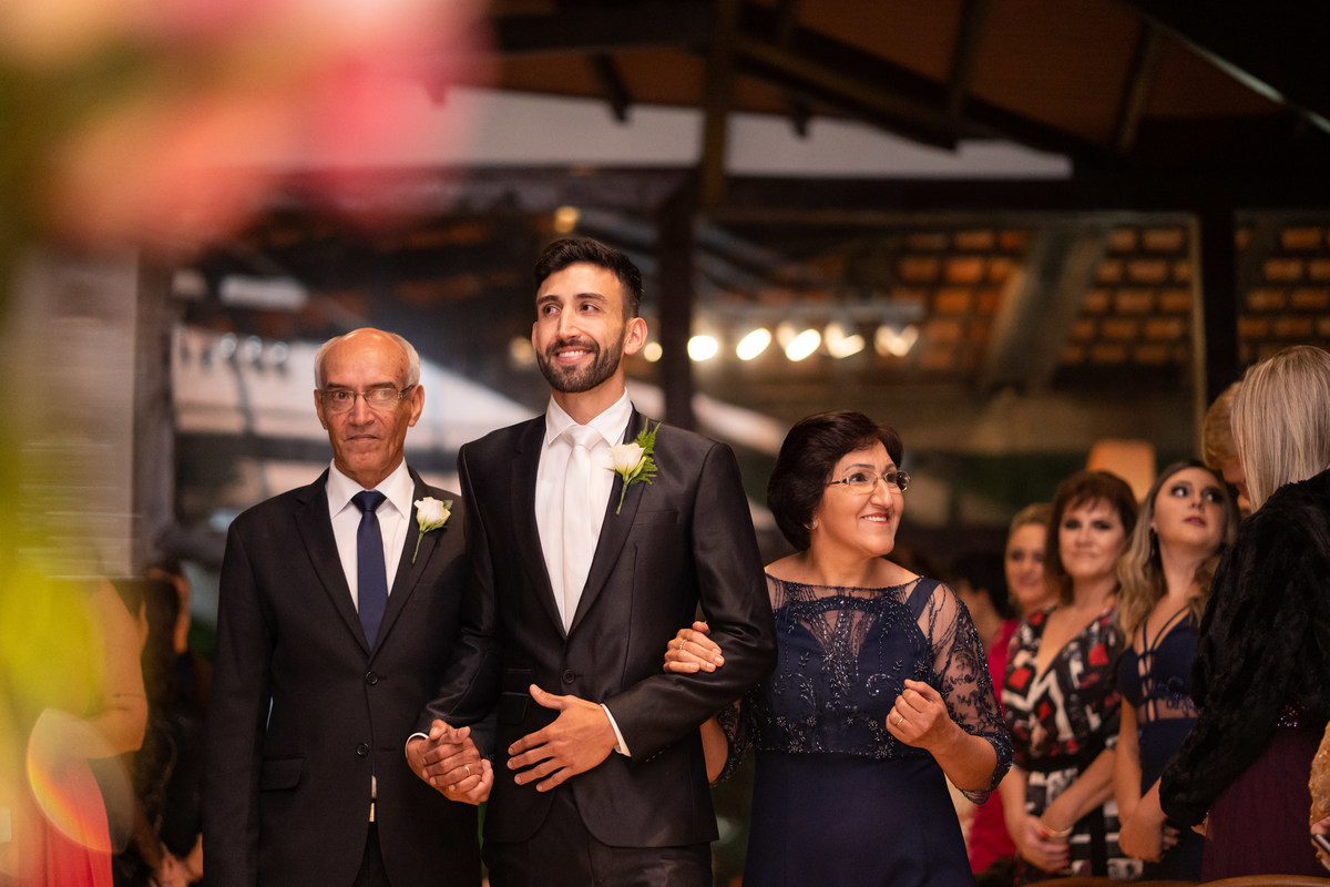 Fotografia de Casamento em Curitiba Rebeca e Vinicius no Magiiore Barigui. Entrada do noivo sorrindo com os pais. Fotografado pelo fotógrafo de casamento Michel Druziki