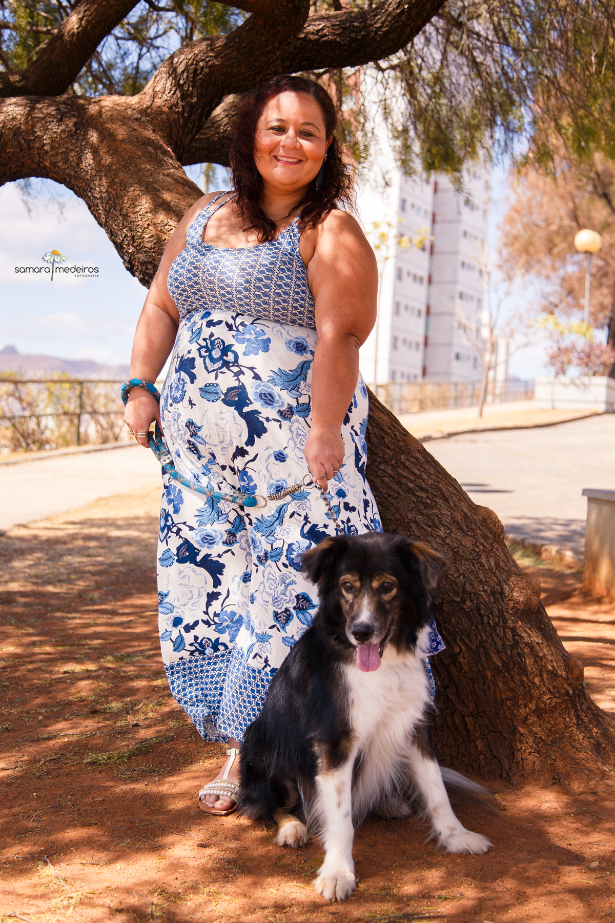 Mulher de pé em frente a uma árvore segurando seu cão border collie e ambos olhando para a câmera, posando.