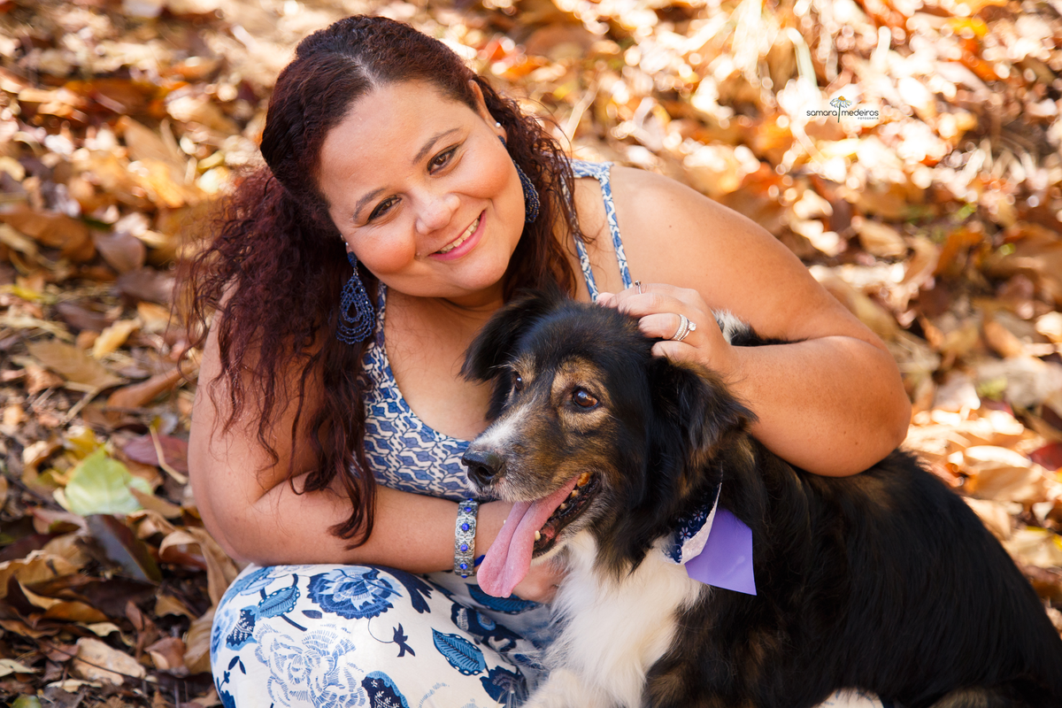 Close em uma mulher sentada no chão com seu cachorro border collie no colo, o cão com a língua para fora e a mulher sorrindo para a foto.