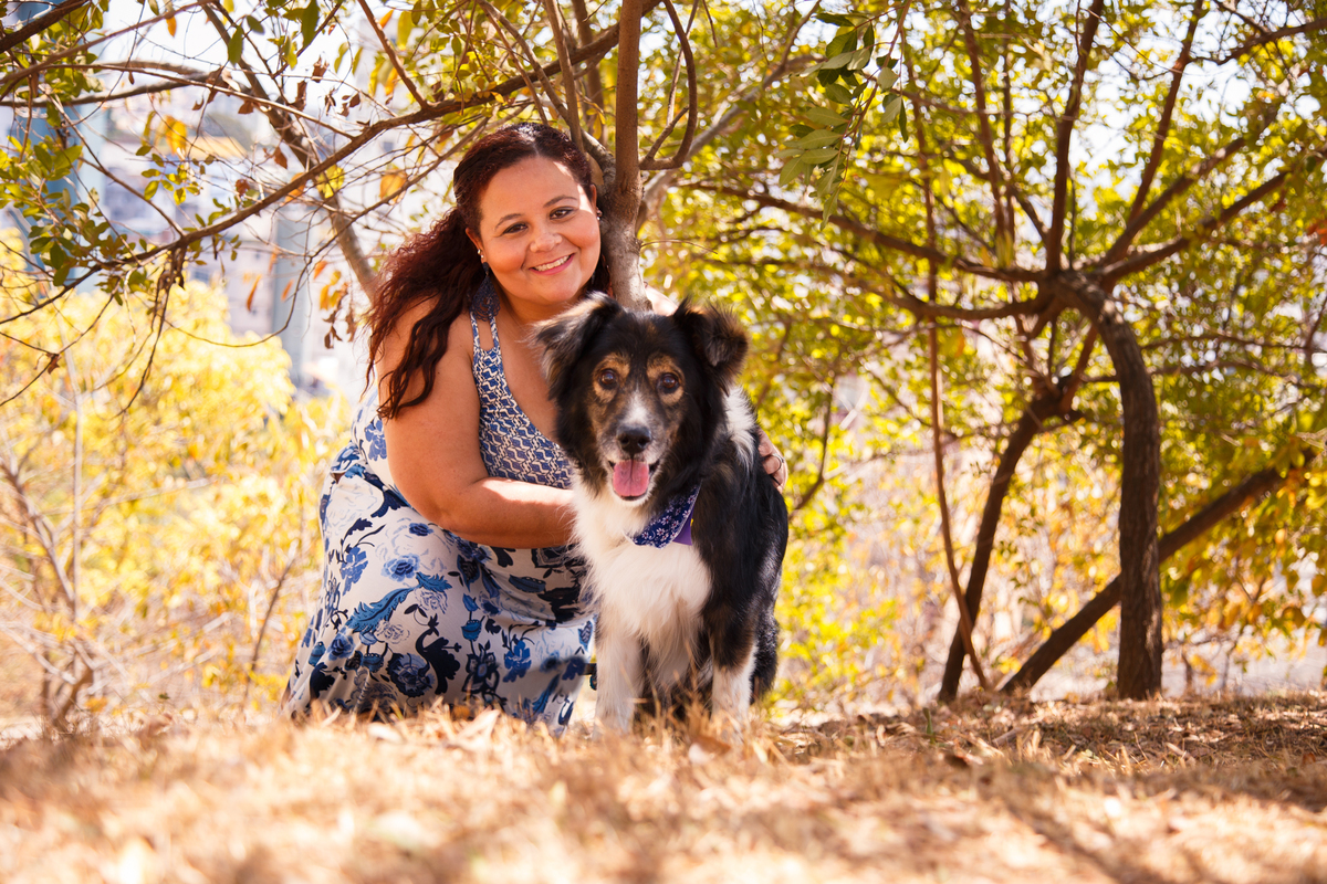 Mulher com seu cachorro border collie, ambos olhando para a câmera, o cão com a língua para fora, em meio a árvores e verde em parque de Belo Horizonte.
