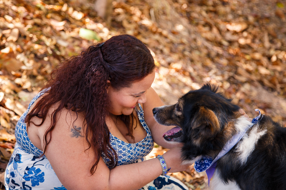 Mulher sentada no chão coberto de folhas secas olhando nos olhos de seu cachorro border collie idoso e sorrindo.