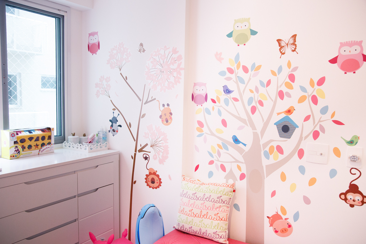 Decoração do quarto de uma bebê com decalques de árvore e animais colados na parede.