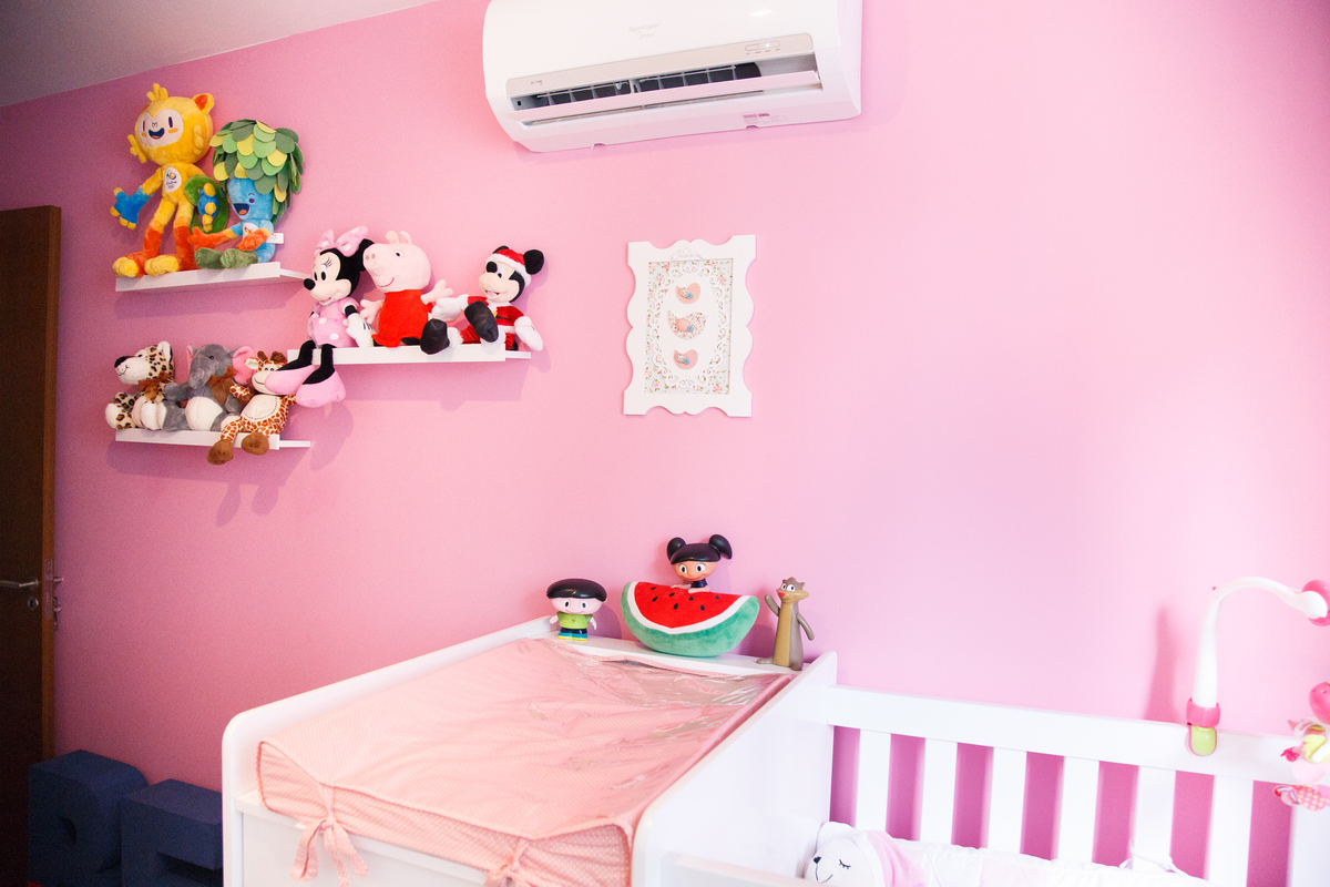 Detalhes da decoração do quarto de uma bebê com prateleiras, bonecos e bichinhos de pelúcia e o berço branco no canto da imagem.