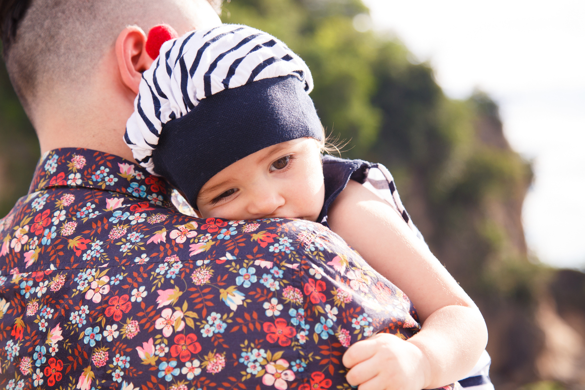 Bebê deitada no ombro de seu pai, cansada após ensaio de fotos, quase dormindo.