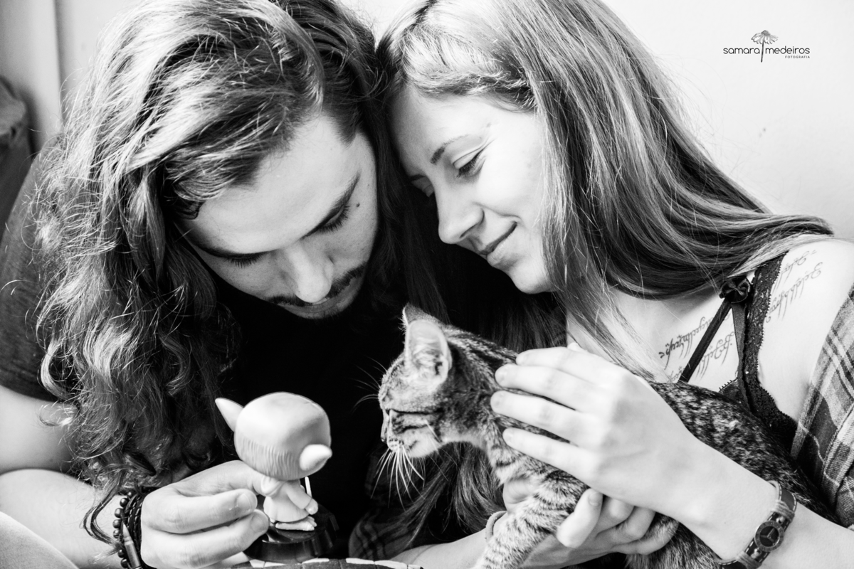 Foto em preto e branco de um casal brincando com sua gatinha tigrada e um pop do Yoda.