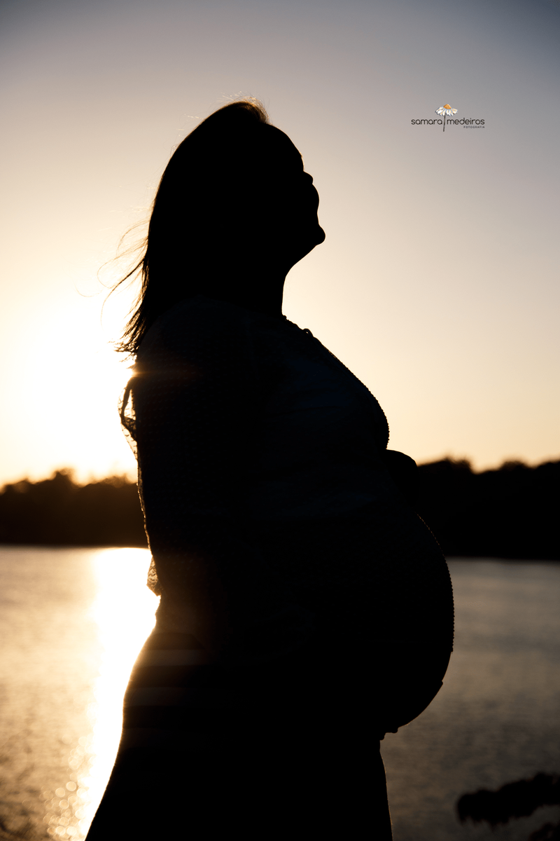 Gestante contra a luz formando uma silhueta com a lagoa da Pampulha ao fundo.