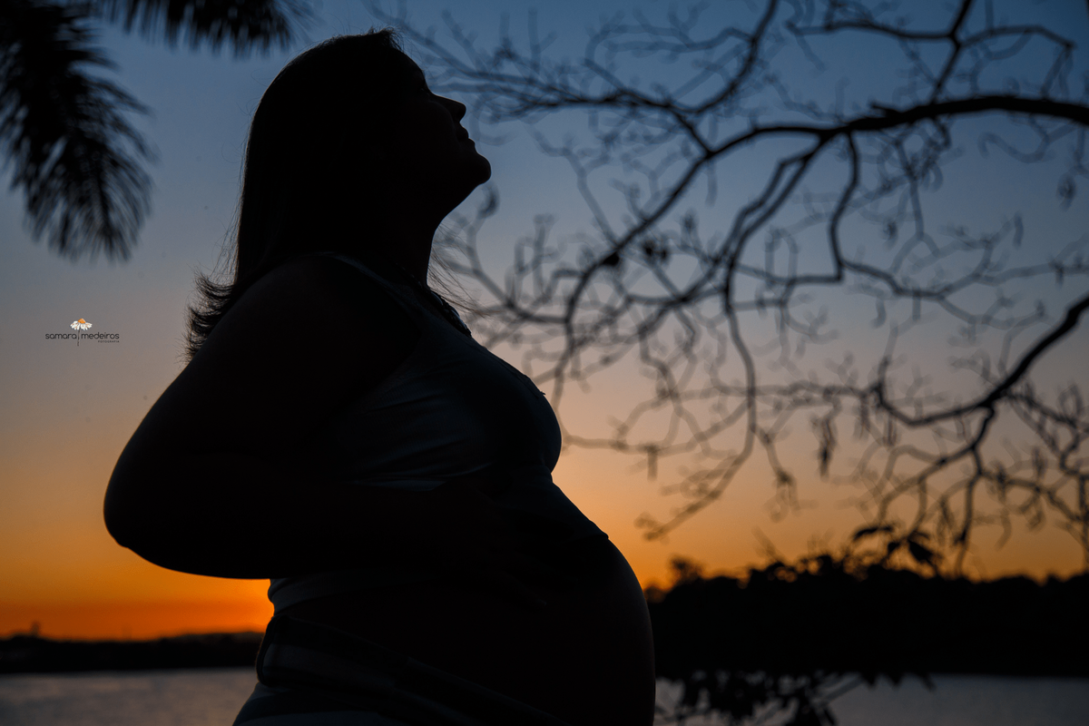 Gestante na contra-luz com um por do sol ao fundo na orla da lagoa da Pampulha.