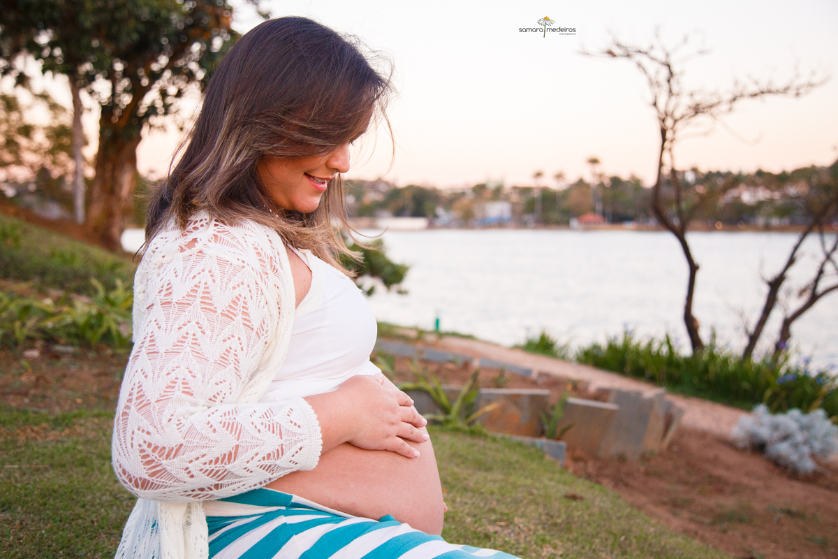 Gestante sentada na grama na orla da Lagoa da Pampulha acariciando Gestante sentada na grama na orla da Lagoa da Pampulha acariciando e olhando para a barriga com um sorriso.