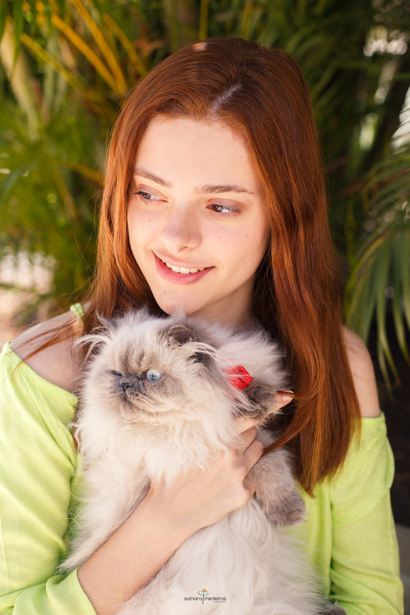 Menina abraçando seu gato persa himalaio, ambos olhando para o lado.