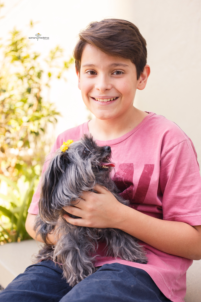 Menino segurando sua cachorrinha yorkshire no colo enquanto sorri para a câmera.