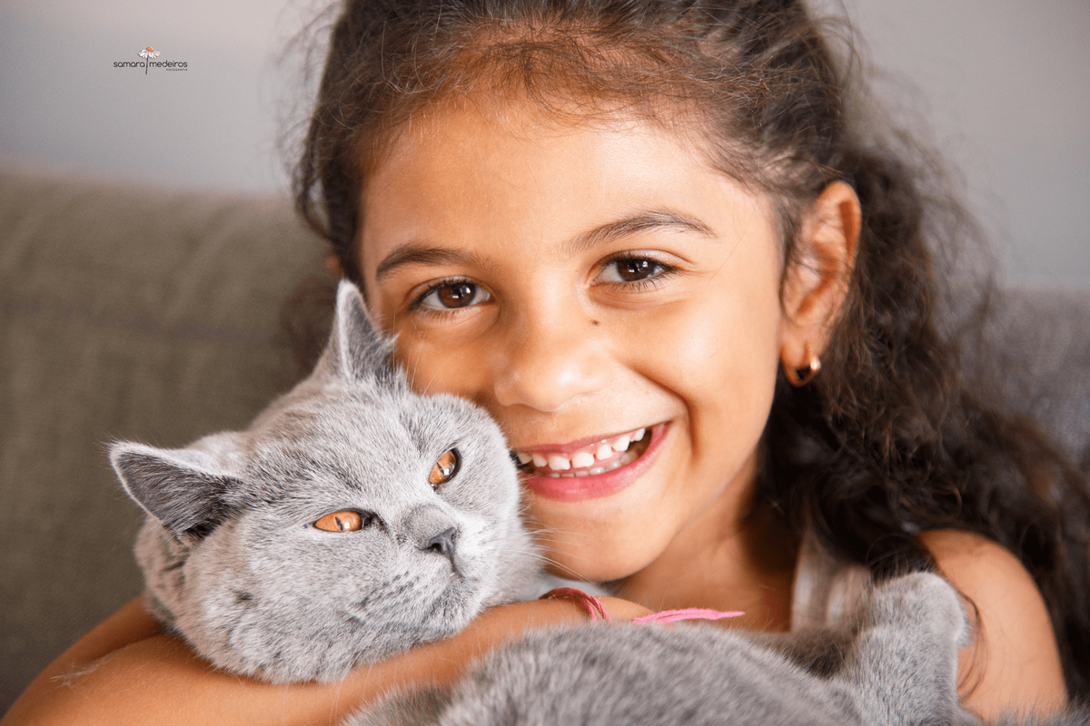 Close no rosto de uma menina carregando uma gatinha cinza no colo, abraçando próxima ao rosto.