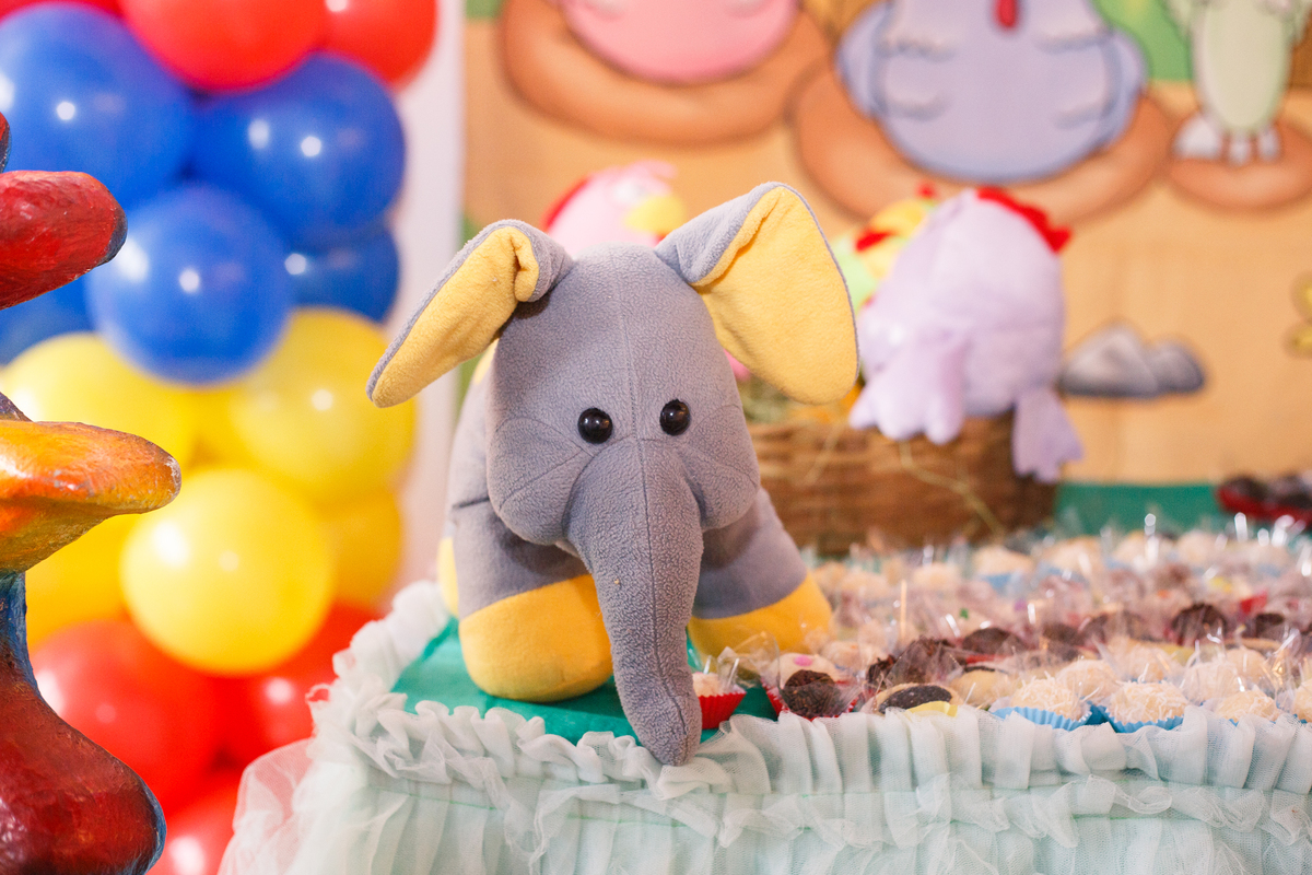 Detalhe da mesa do bolo em aniversário infantil no tema Galinha Pintadinha, com um elefante de pelúcia.