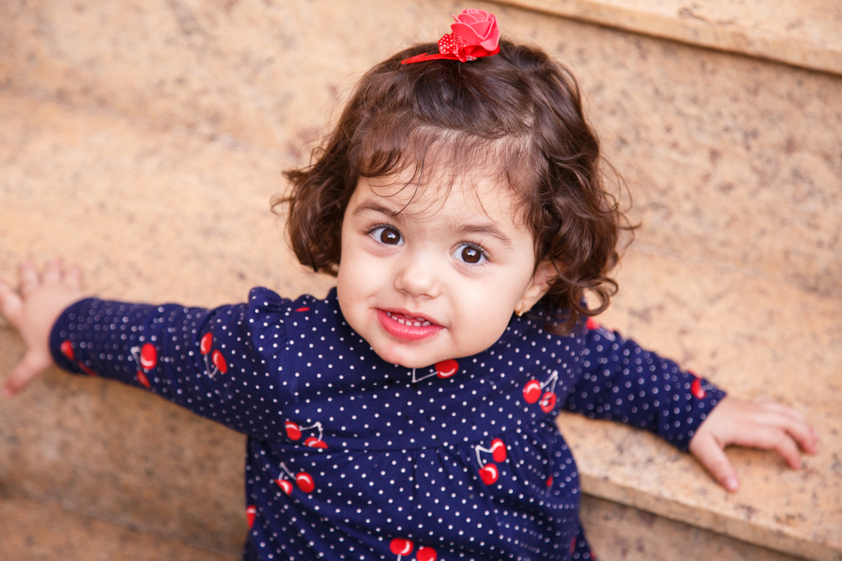 Criança sorrindo apoiada no degrau de uma escada e olhando para a câmera.