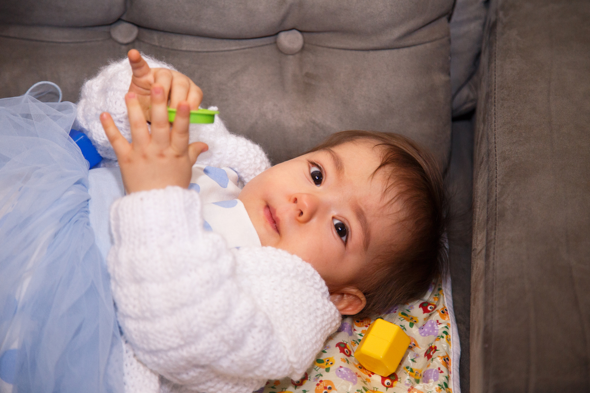 Bebê de um ano deitada em um sofá durante aniversário de 1 ano, olhando para a câmera.