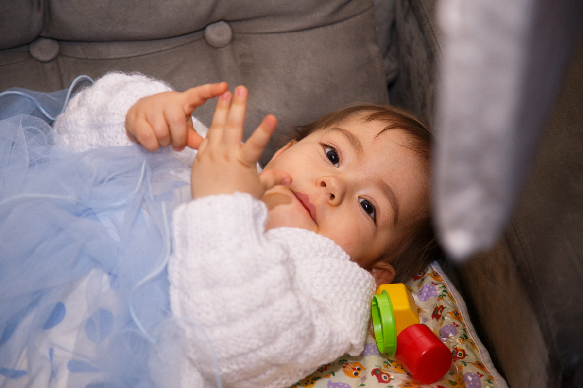Bebê de 1 ano em seu aniversário de 1 ano deitada em um sofá e mexendo os dedinhos.