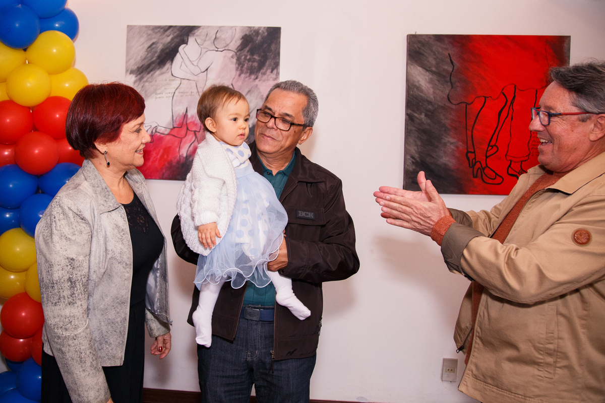 Bebê de 1 ano no colo do avó com sua avó atrás e o outro avó fazendo gracinhas, chamando para o colo.
