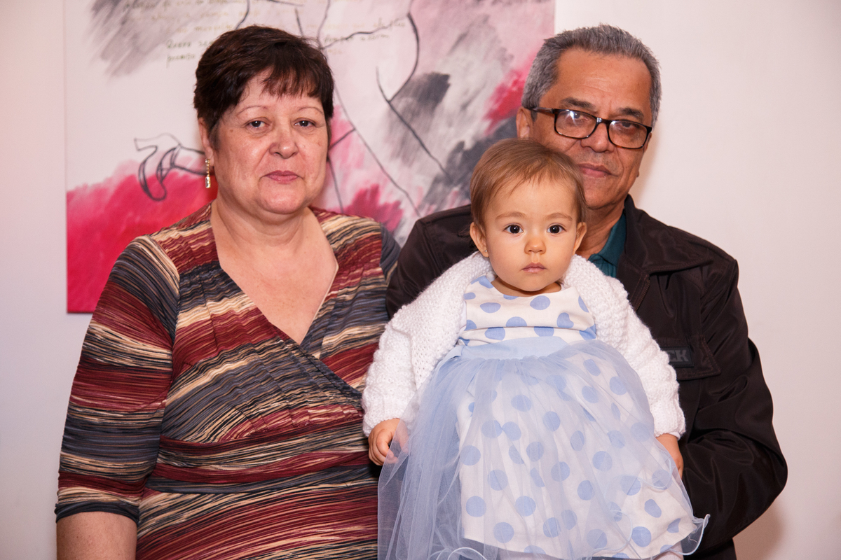 Avó e avô maternos posando para foto com a netinha em seu aniversário de 1 ano.
