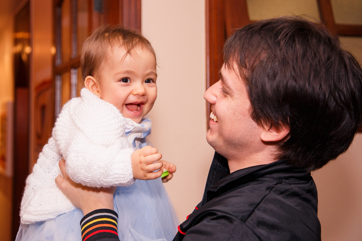 Pai brincando com sua bebê durante seu aniversário infantil, ambos sorrindo.