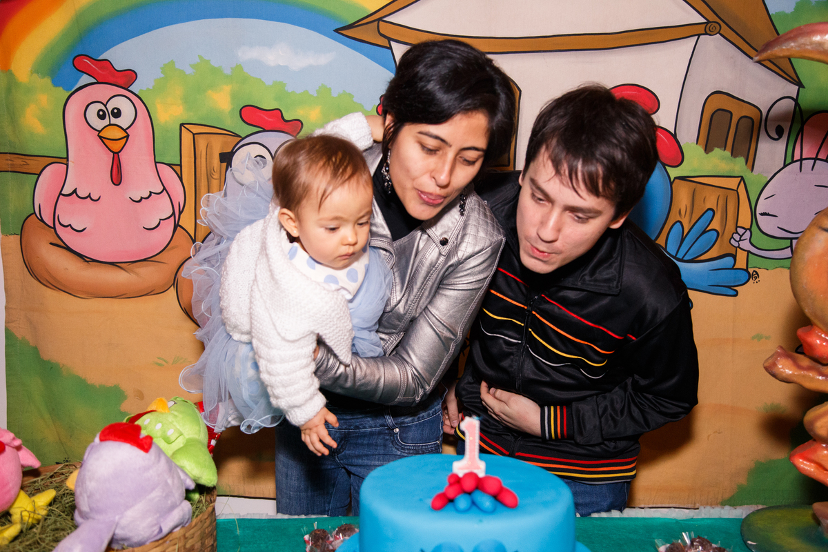 Família atrás da mesa do bolo assoprando a velinha após parabéns durante aniversário infantil.