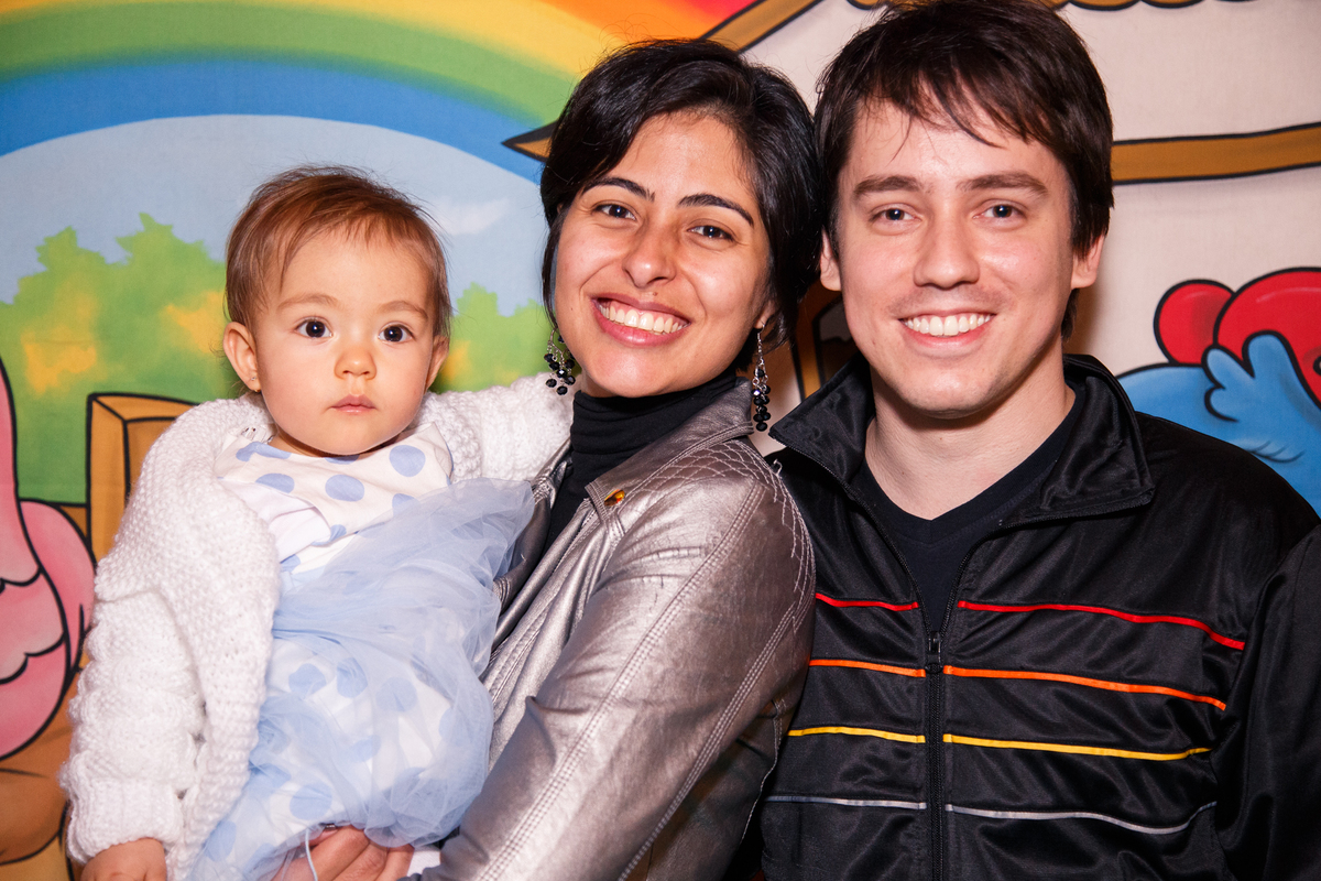 Mãe, pai e bebê posando para foto durante aniversário infantil de 1 ano.