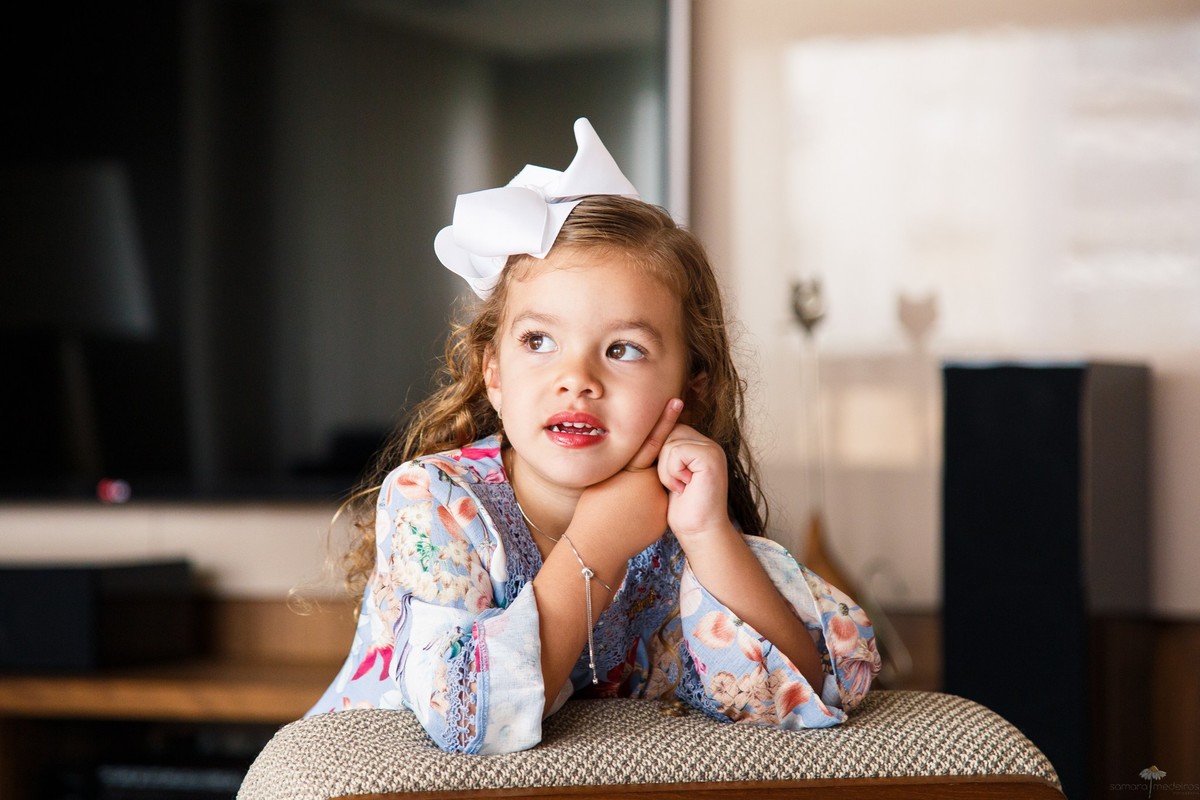 Criança posando para foto na sala de sua casa, encostada no sofá e olhando para o lado.