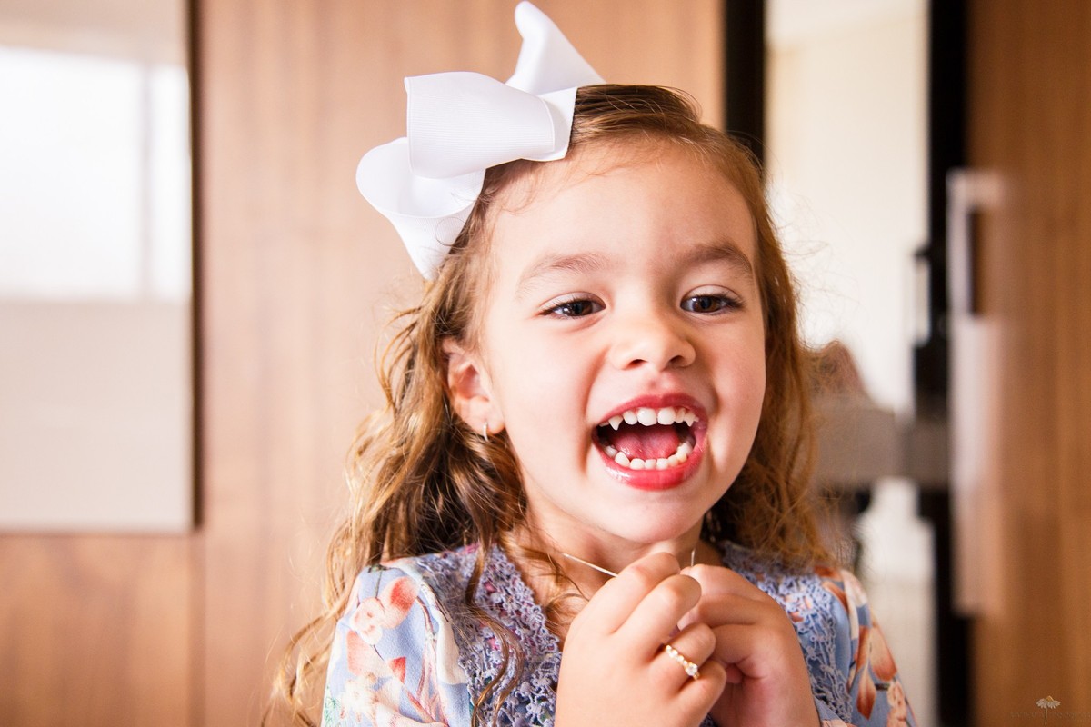 Close no rosto de uma criança que está brincando com o pingente do colar e gargalhando.