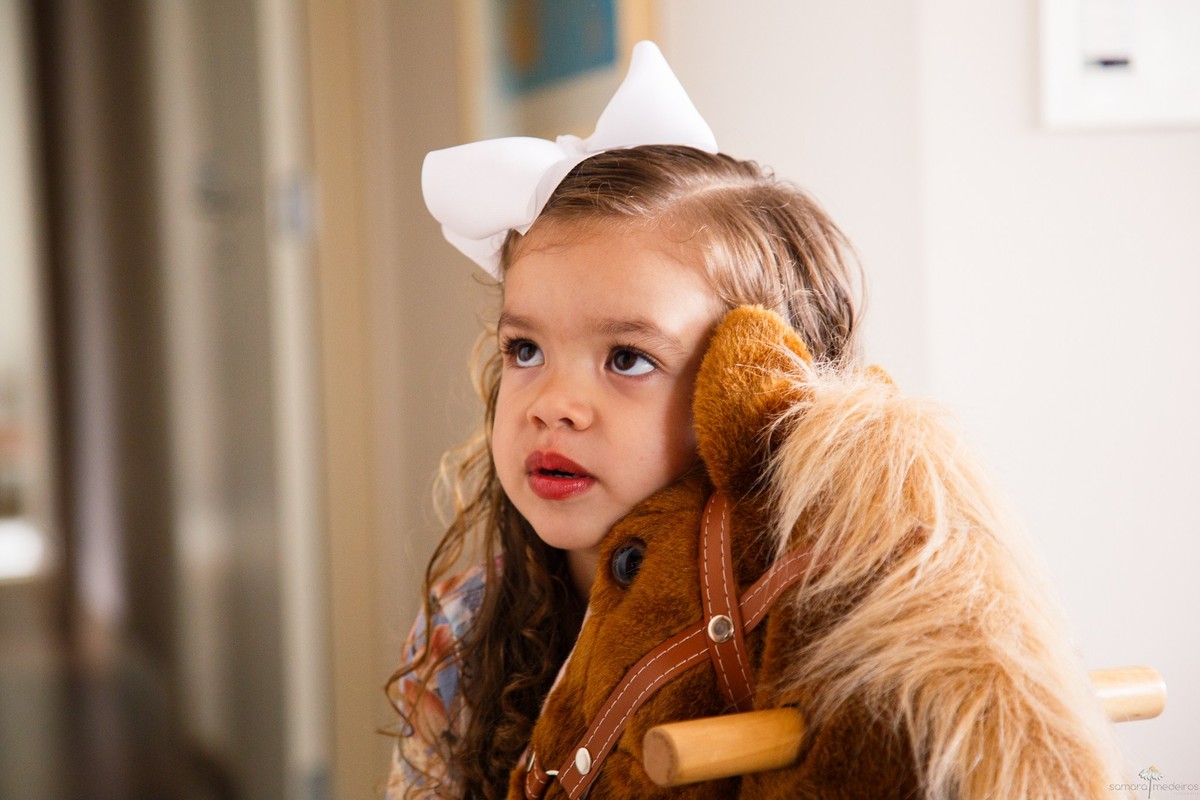 Criança olhando na diagonal contrária à foto e abraçando um cavalo de pelúcia.