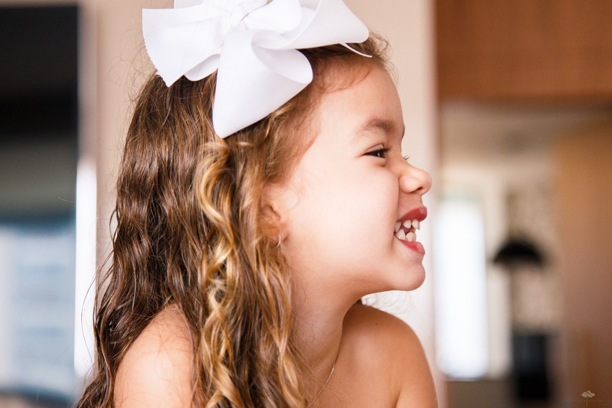 Close de uma criança de perfil sorrindo, mostrando os dentes durante sessão fotográfica infantil.