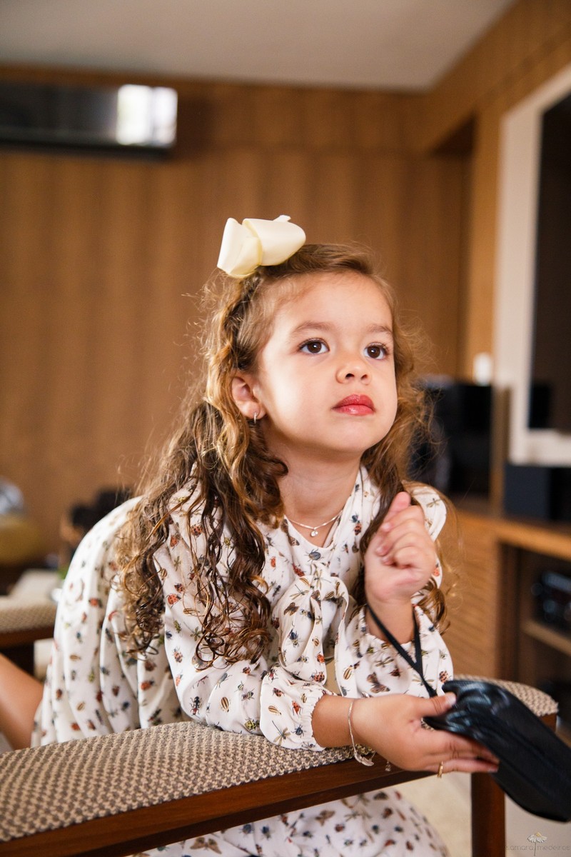 Criança séria debruçada no encosto do sofá olhando para a mãe que não aparece na foto, durante sessão fotográfica infantil.