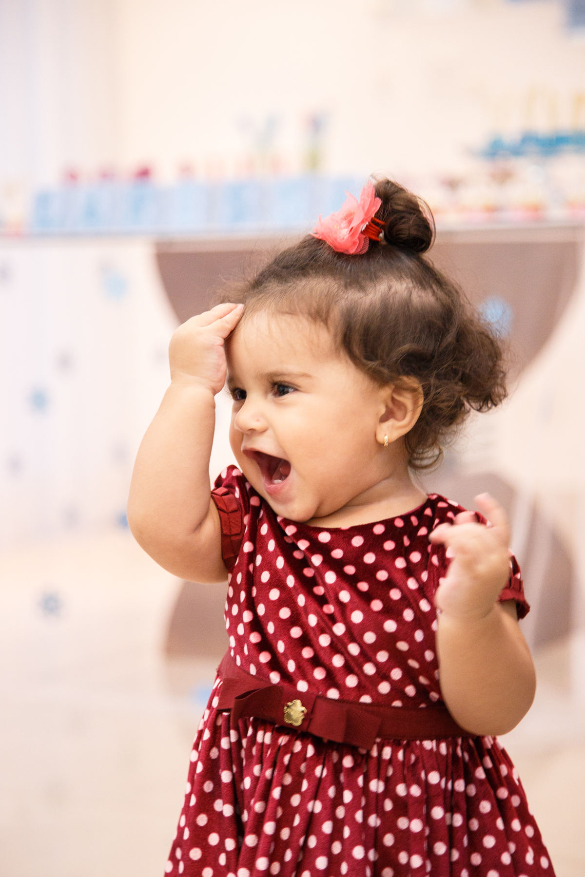 Bebê de um ano fazendo careta e batendo a mãozinha na testam sorrindo.