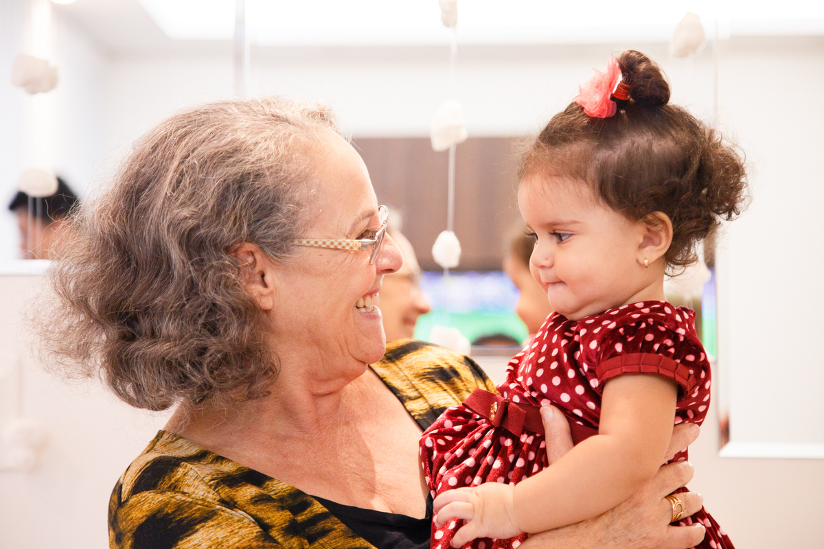 Bebê no colo da avó, as duas se olhando, em seu aniversário de 1 ano.