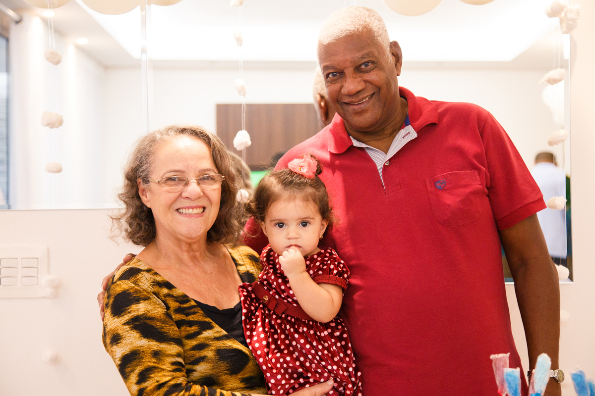 Bebê aniversariante em seu aniversário de 1 ano, atrás da mesa do colo com sua avó e avô.