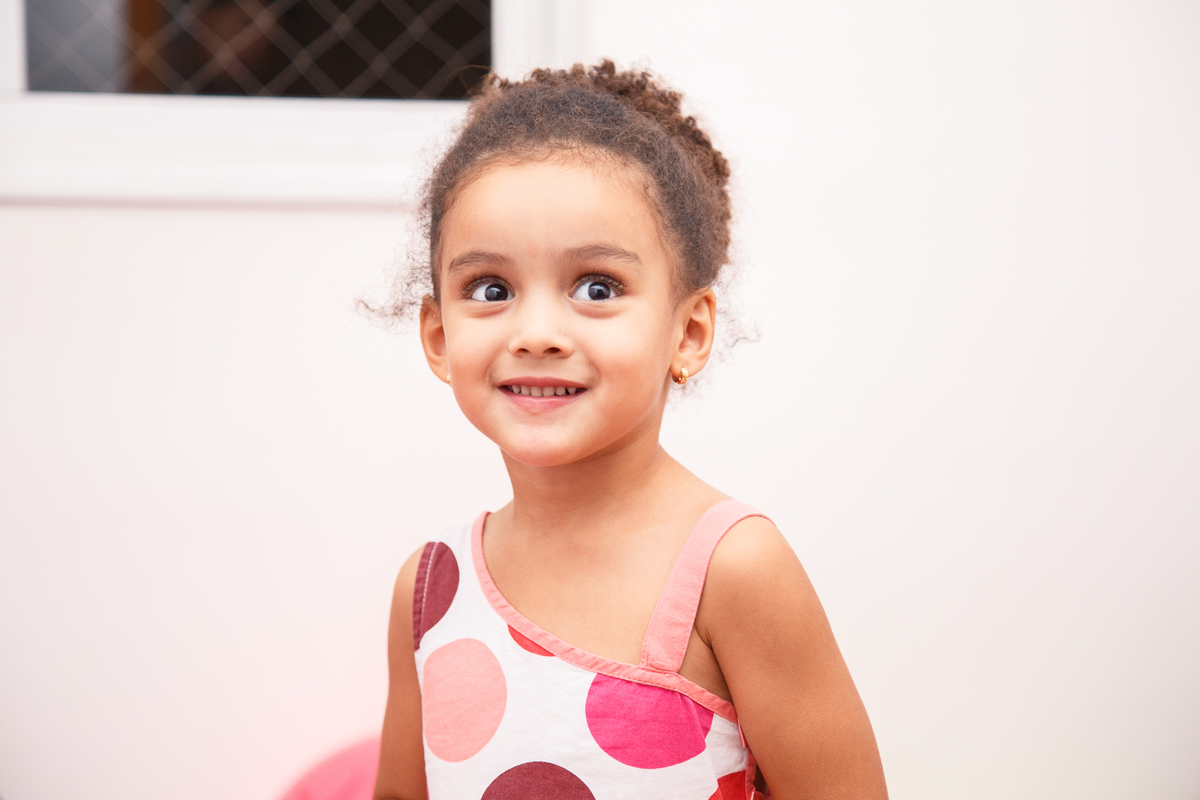 Close de uma criança no aniversário de 1 ano de sua irmã, sorrindo e olhando para alguém atrás da fotógrafa.