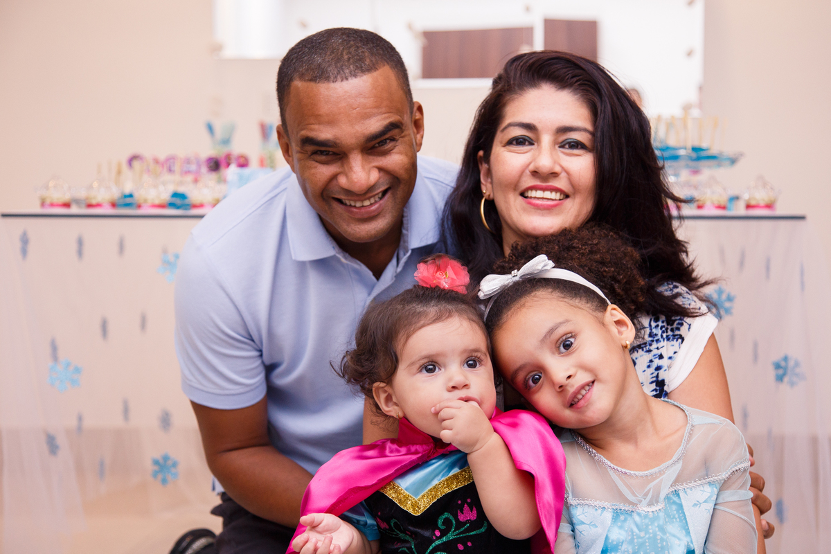 Pai e mãe com suas duas filhas fantasiadas de Anna e Elsa do Frozen durante aniversário infantil.