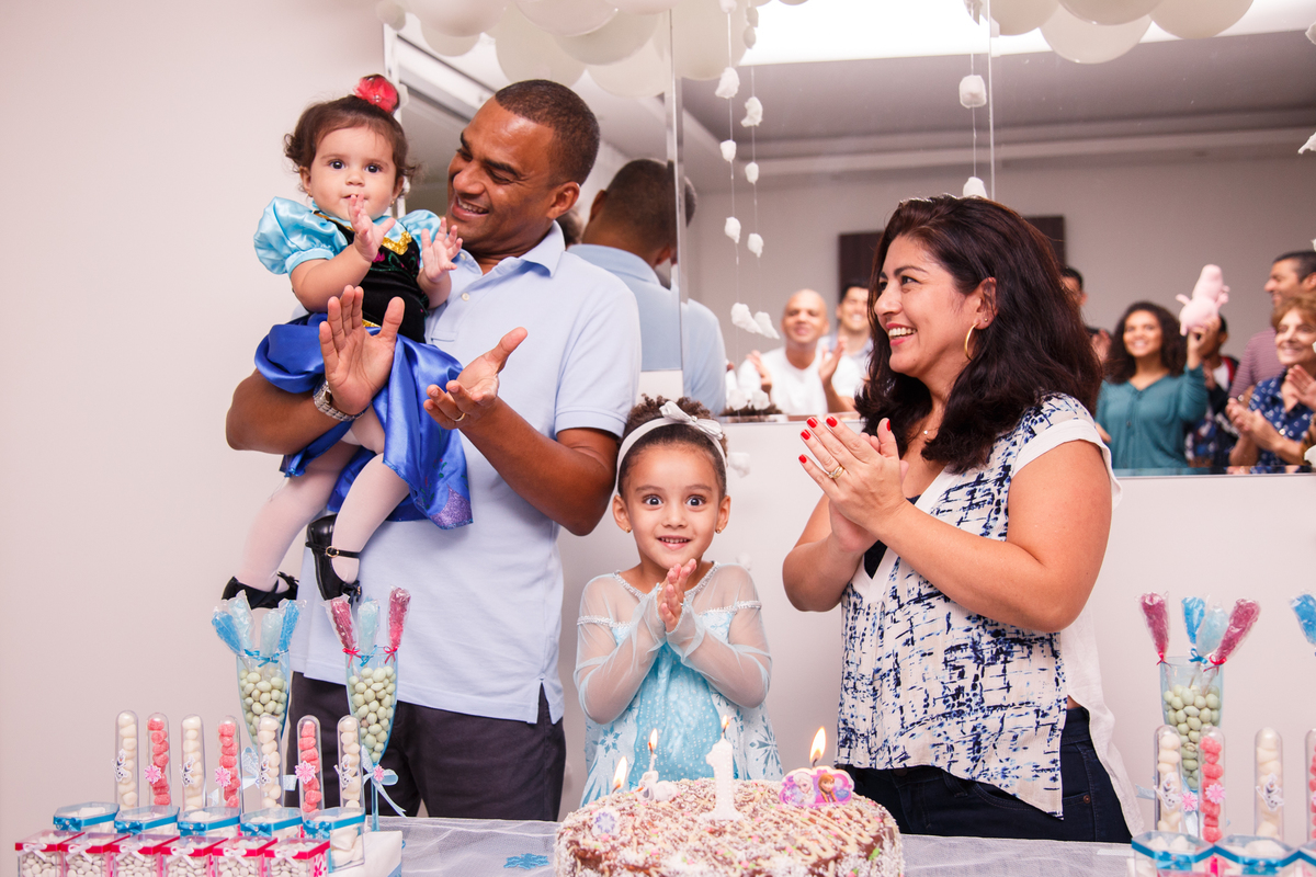 Família atrás da mesa do bolo cantando parabéns em aniversário de 1 ano.
