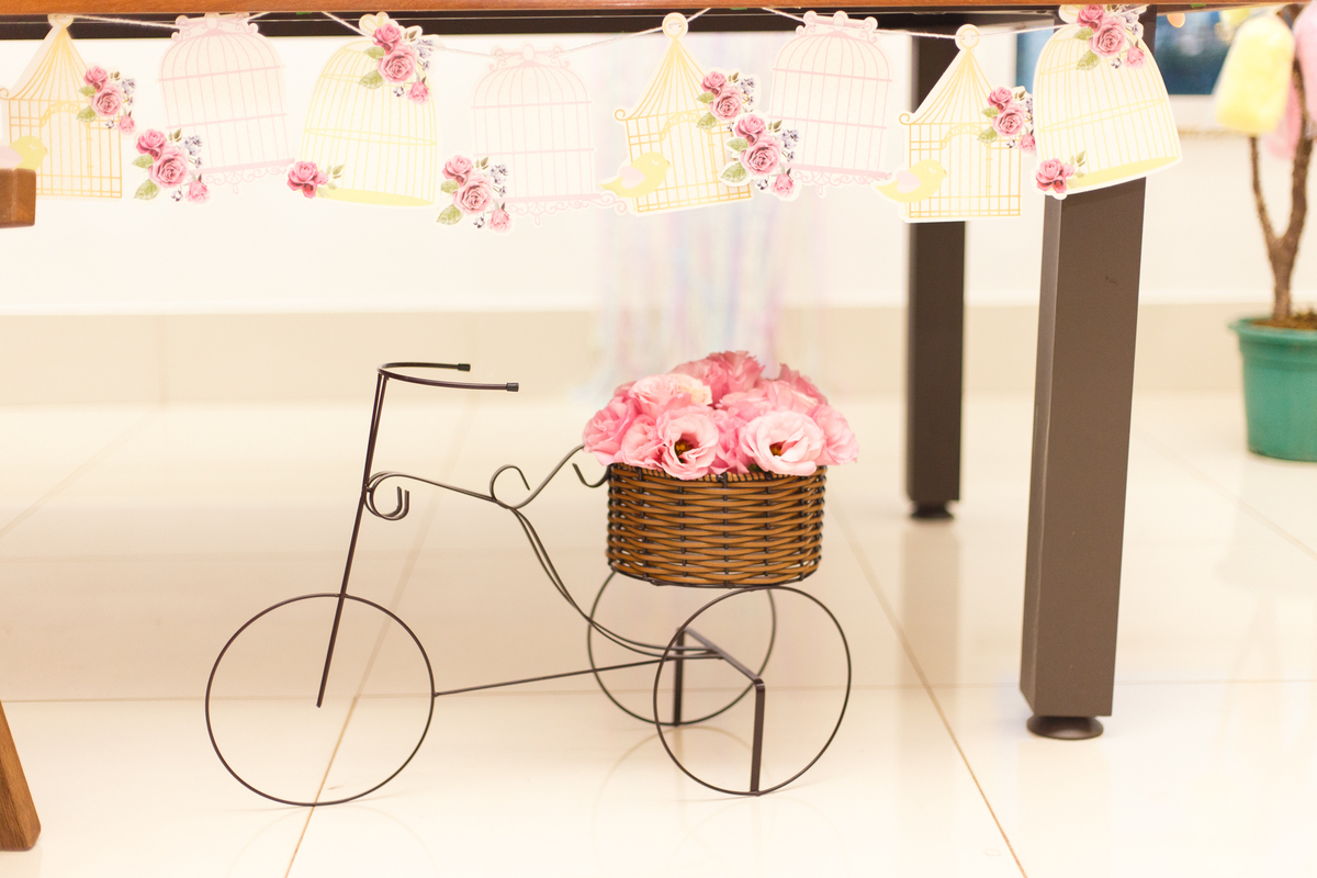 Detalhe da decoração de um aniversário infantil no tema fazendinha, uma bicicleta de ferro em miniatura com um cesto de flores na garupa.