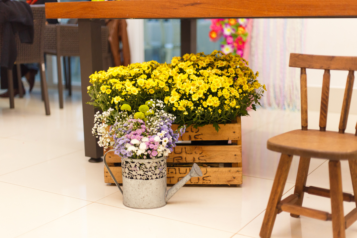 Detalhe da decoração de um aniversário infantil no tema fazendinha, com um cesto de flores amarelas e um regador ao lado.
