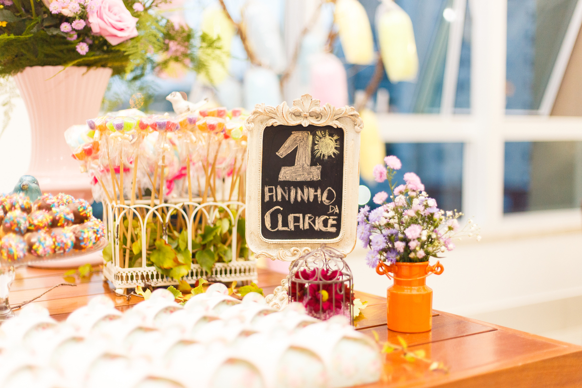 Detalhe da mesa do bolo de um aniversário infantil de 1 ano no tema fazendinha, com alguns doces e uma plaquinha com o nome da aniversariante.