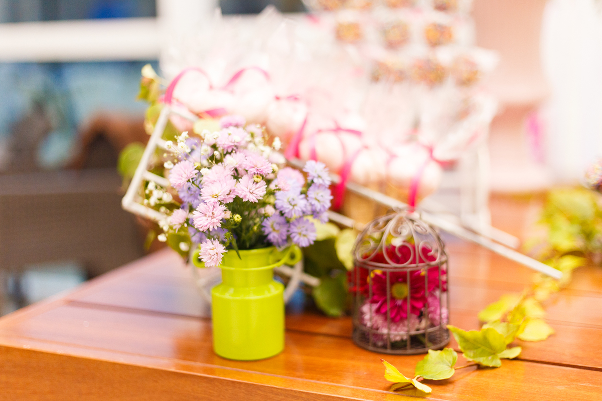 Detalhe da decoração da mesa de bolo de um aniversário infantil com o tema fazendinha, com um 
mini carrinho de mão cheio de flores.