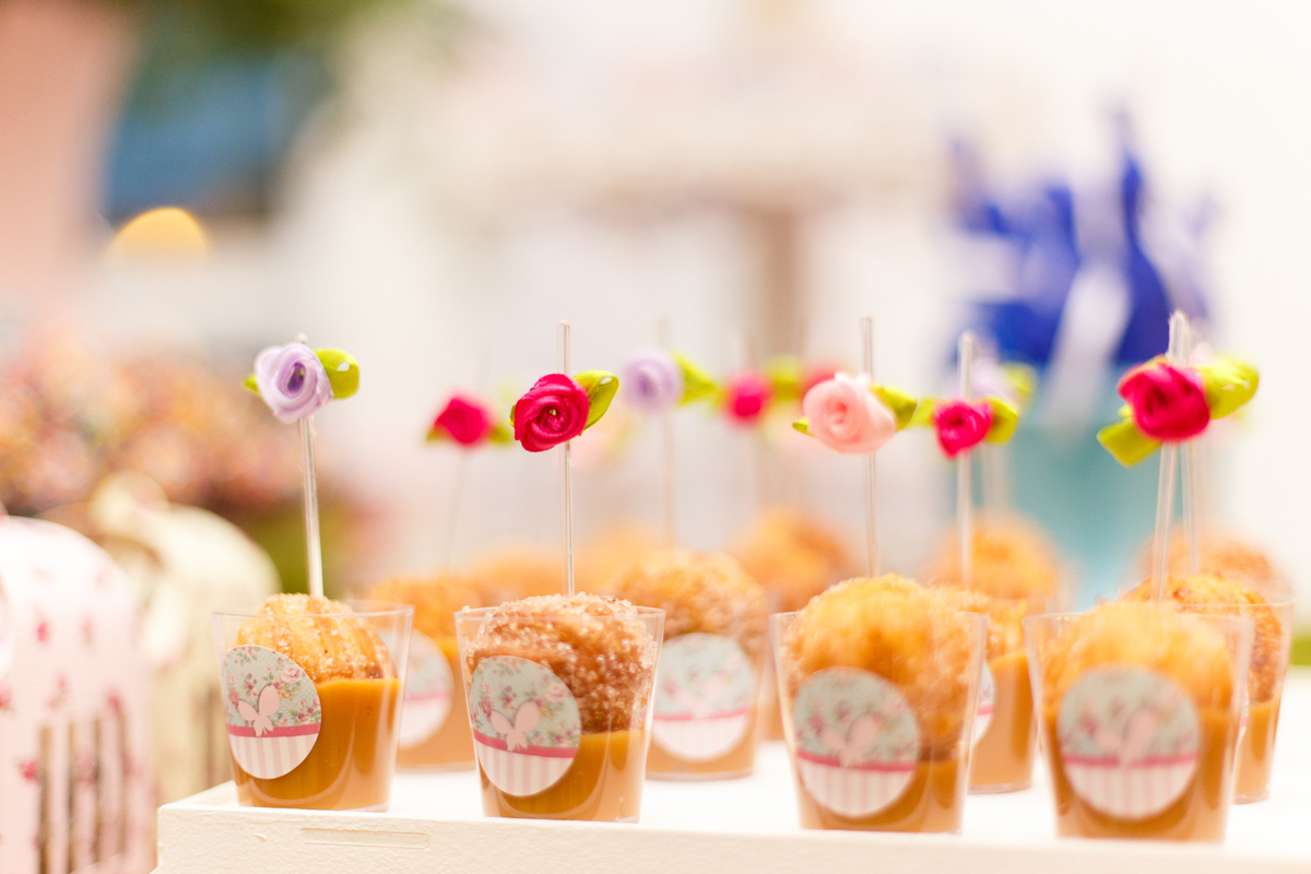 Detalhe de doces de copinho com enfeite de flores em mesa de doces de aniversário infantil.